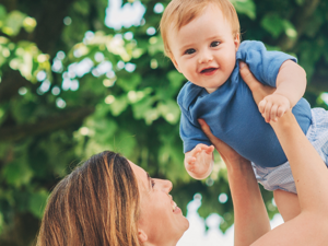 Mother holding baby in the air Infront of trees
