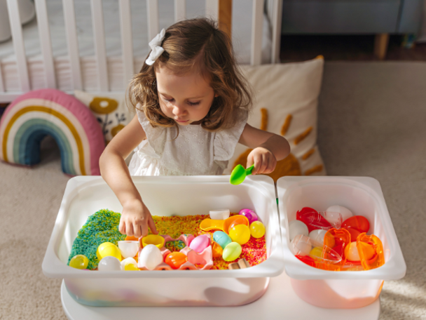 Toddler girl playing with colorful sand and toys