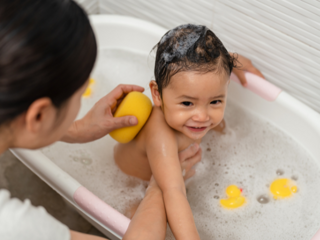 Toddler in a bubble bath with mother holding their body