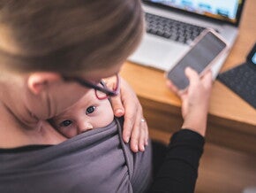 Woman on the phone with baby in grey carrier 