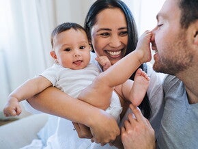 Woman holding her baby while they play with mans face with feet