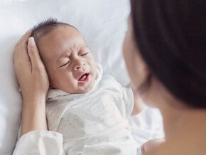 Crying baby in white being comforted by their parent