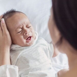 Crying baby in white being comforted by their parent