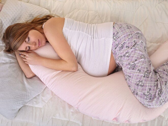 Pregnant woman lying on a bed with pregnancy pillow 
