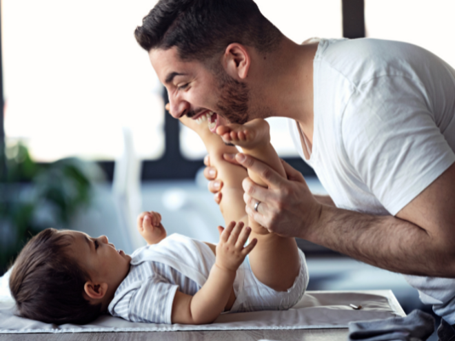 Baby laying down and father making the baby laugh leaning over