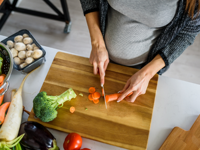 pregnant woman cutting carrot on a wooden chopping board