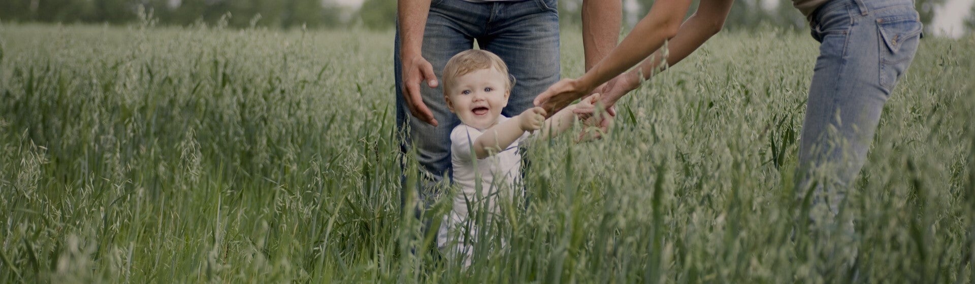 baby holding hands with woman and walking through tall grass