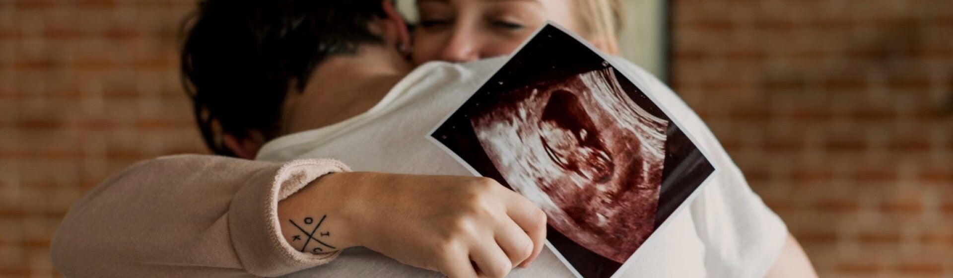 man and woman hugging and holding sonogram image