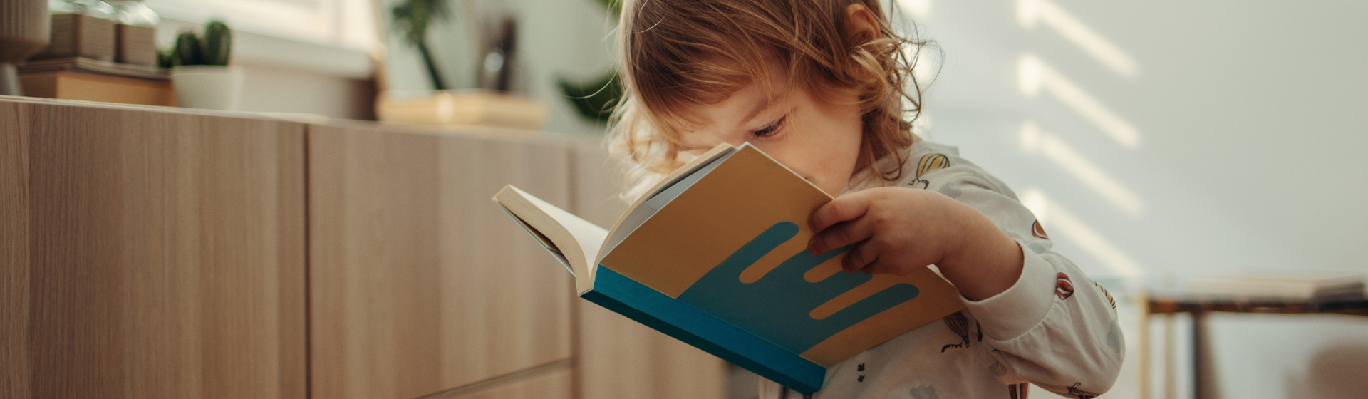 Toddler looking through book in their bedroom wearing onesie