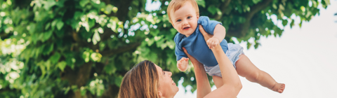 Mother holding baby in the air Infront of trees